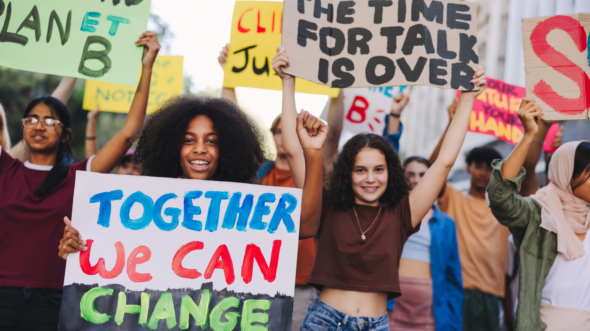 Youth protest against climate change. Group of multicultural youth activists carrying posters and banners while marching against global warming. Happy young people joining the global climate strike.