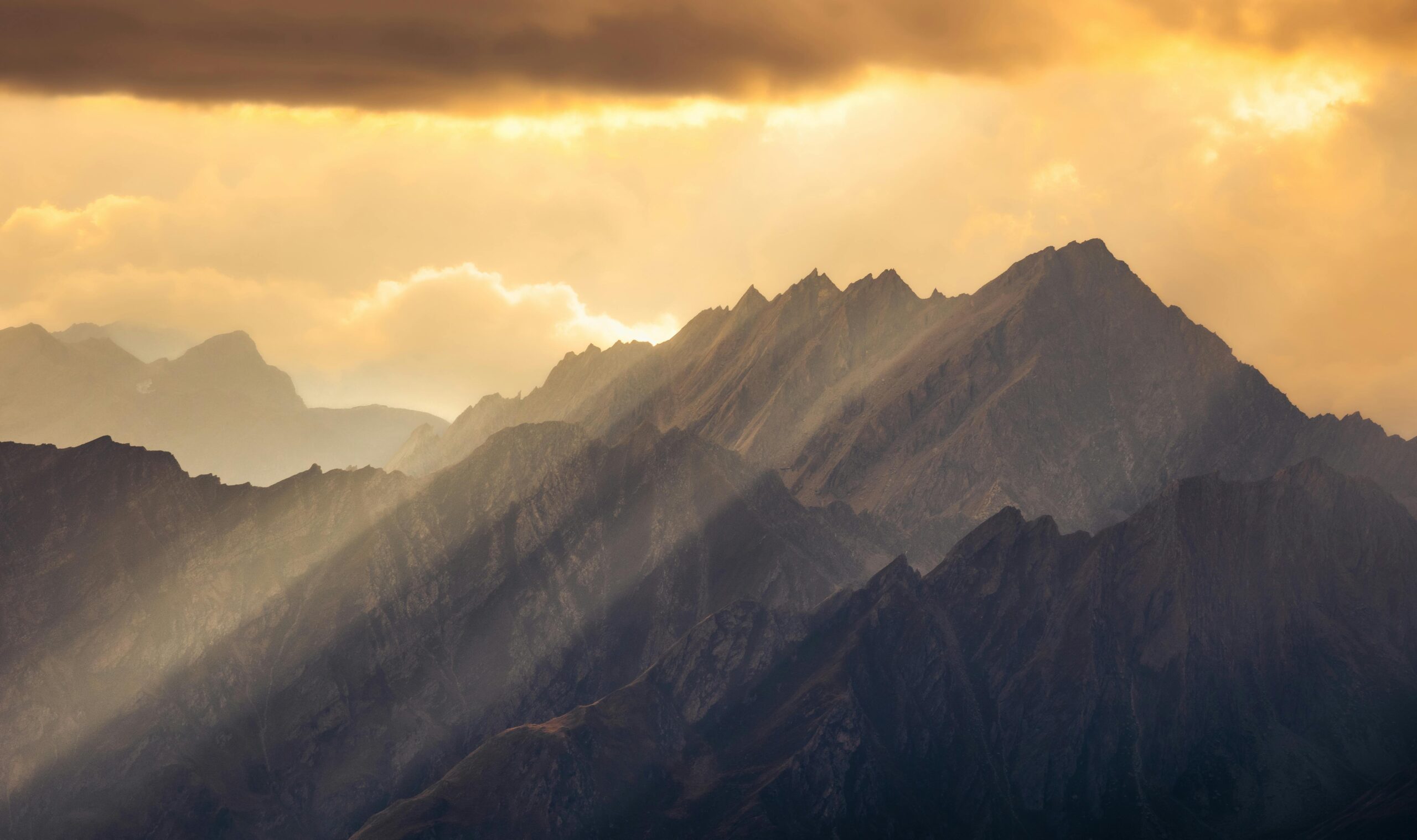 Sunlit rays fall across layered mountain ridges beneath dense cloud.